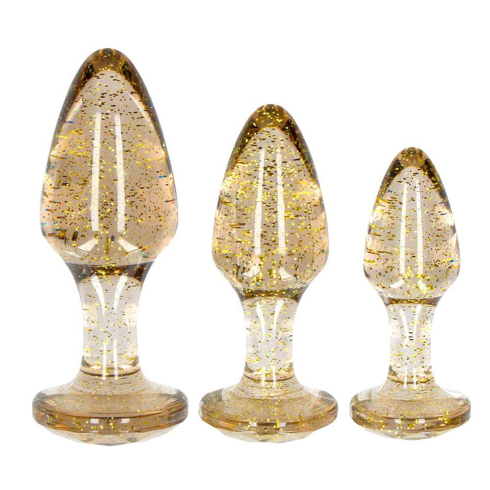 Shots Toys Golden Glitter Akryl Butt Plug Set featuring three shimmering plugs in varying sizes and shapes.