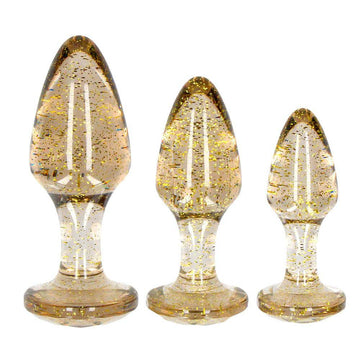 Shots Toys Golden Glitter Akryl Butt Plug Set featuring three shimmering plugs in varying sizes and shapes.